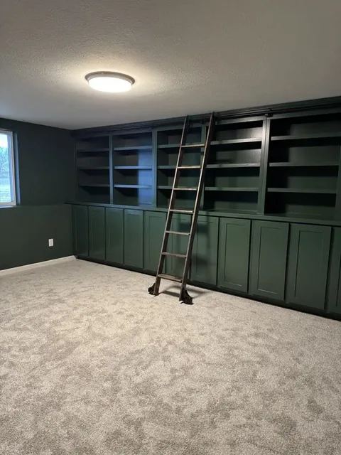 Deep green custom built-in library wall with rolling ladder by Pro Line Finish Carpentry